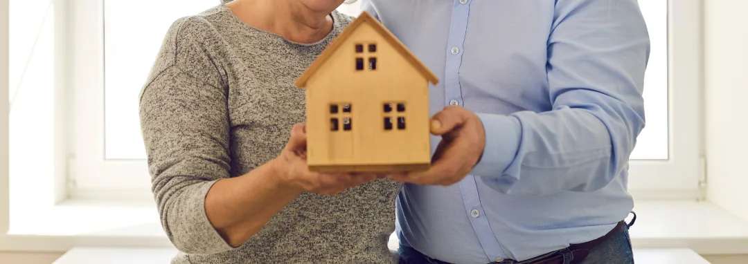 Older couple holding a small wooden model house